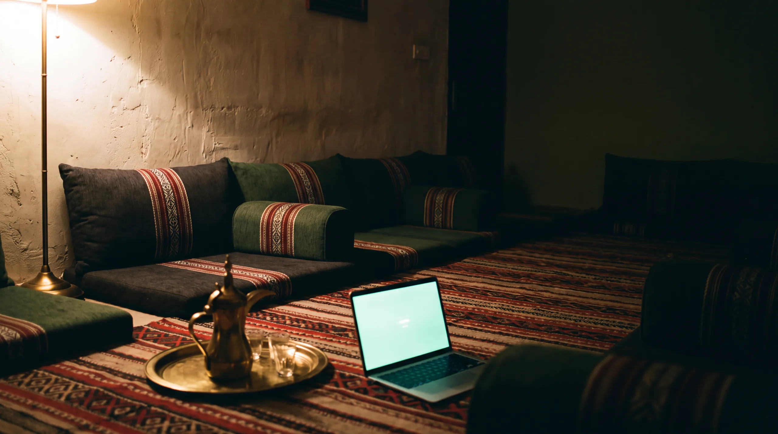 مجلس كويتي في الليل، وجهاز لابتوب على السدو بين دلة القهوة والاستكانات